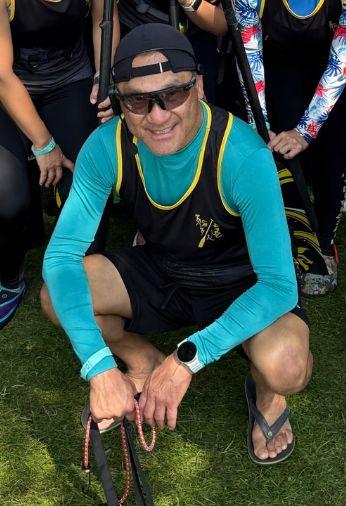 Coach Matthew Ma crouching on the grass with dragon boat paddles